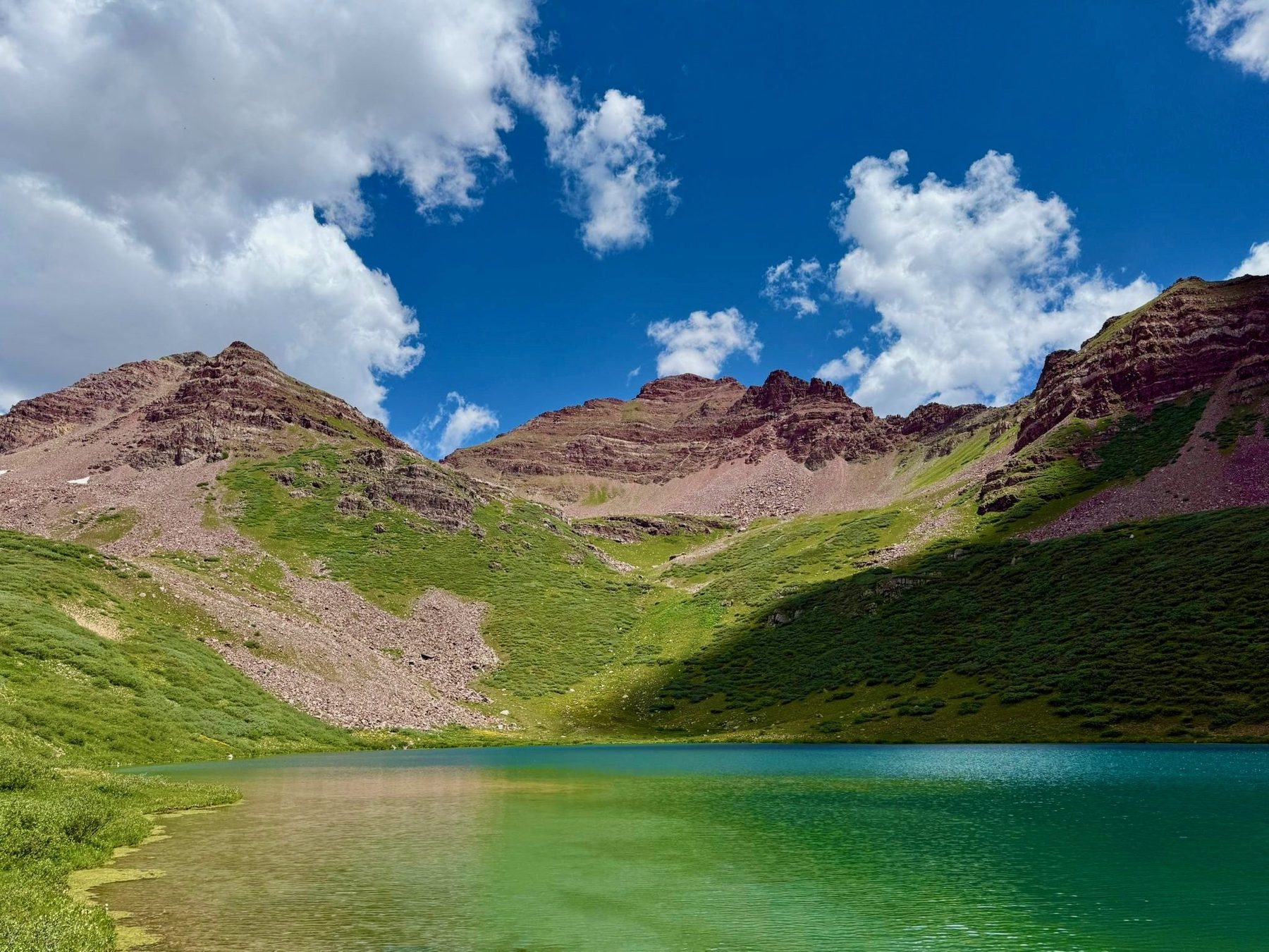 Maroon-red peaks rising above a still turquoise alpine lake